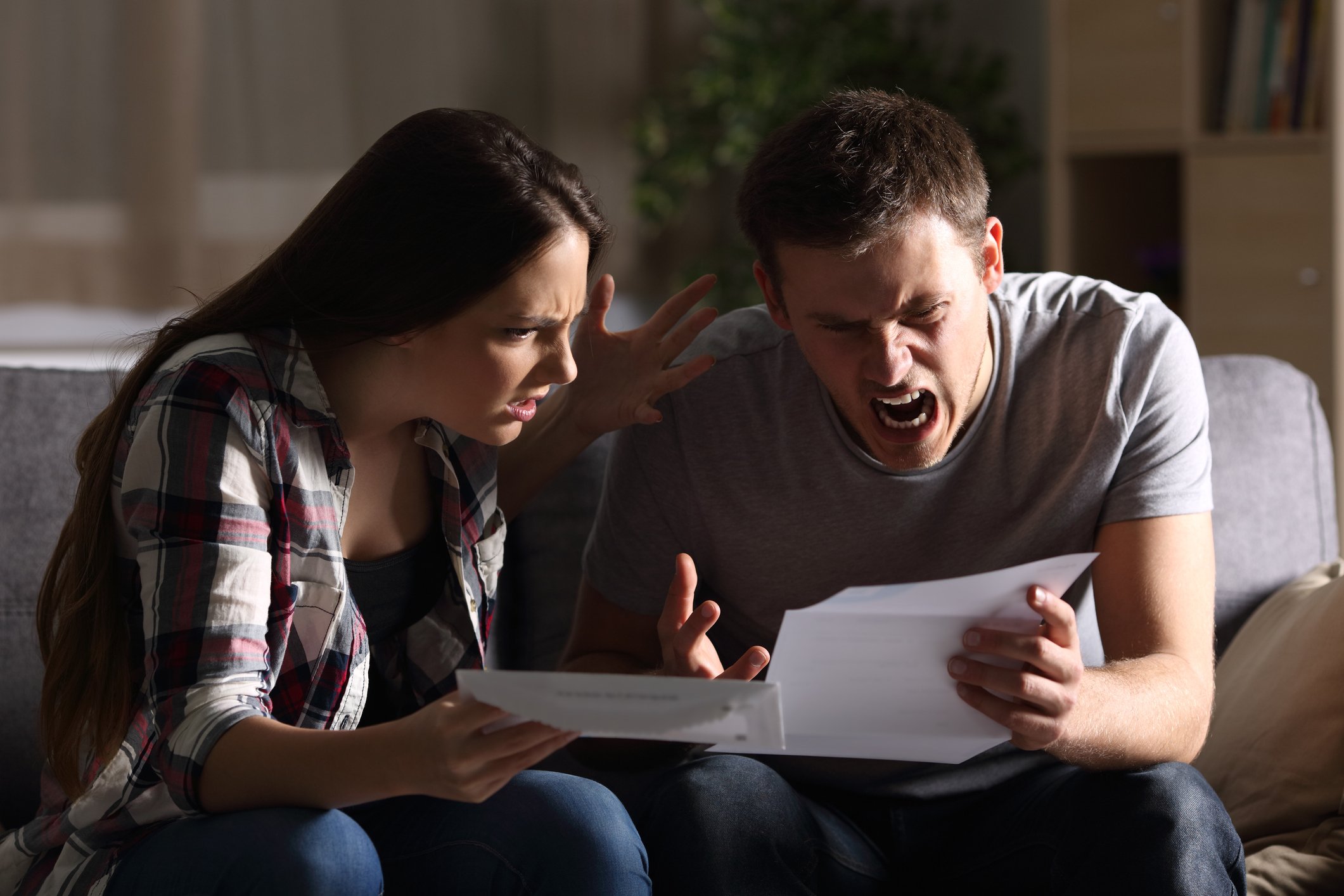 Furious people reading a letter while sitting on a couch. 