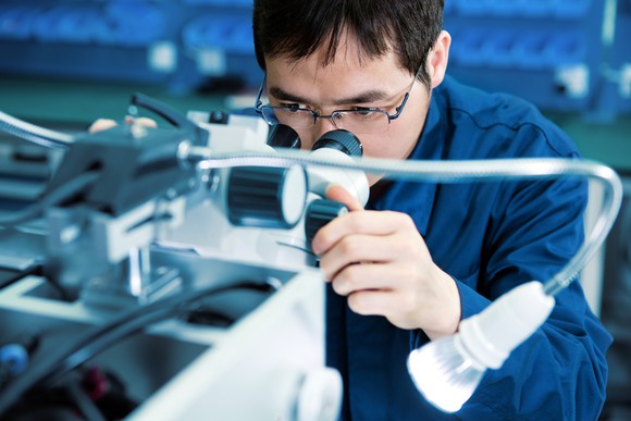Technician examines a semiconductor under a microscope.