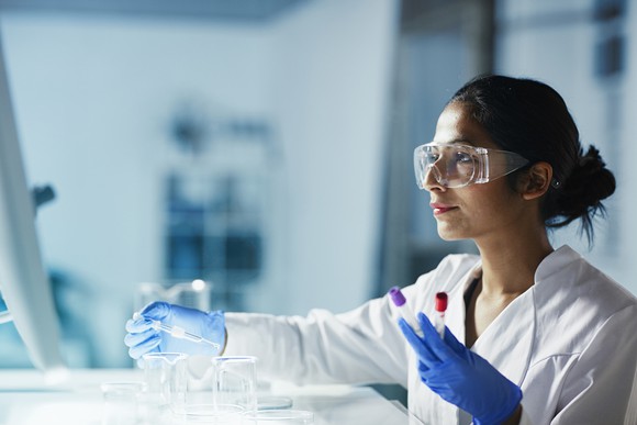 A person wearing a lab coat, gloves, and safety glasses working in a laboratory.
