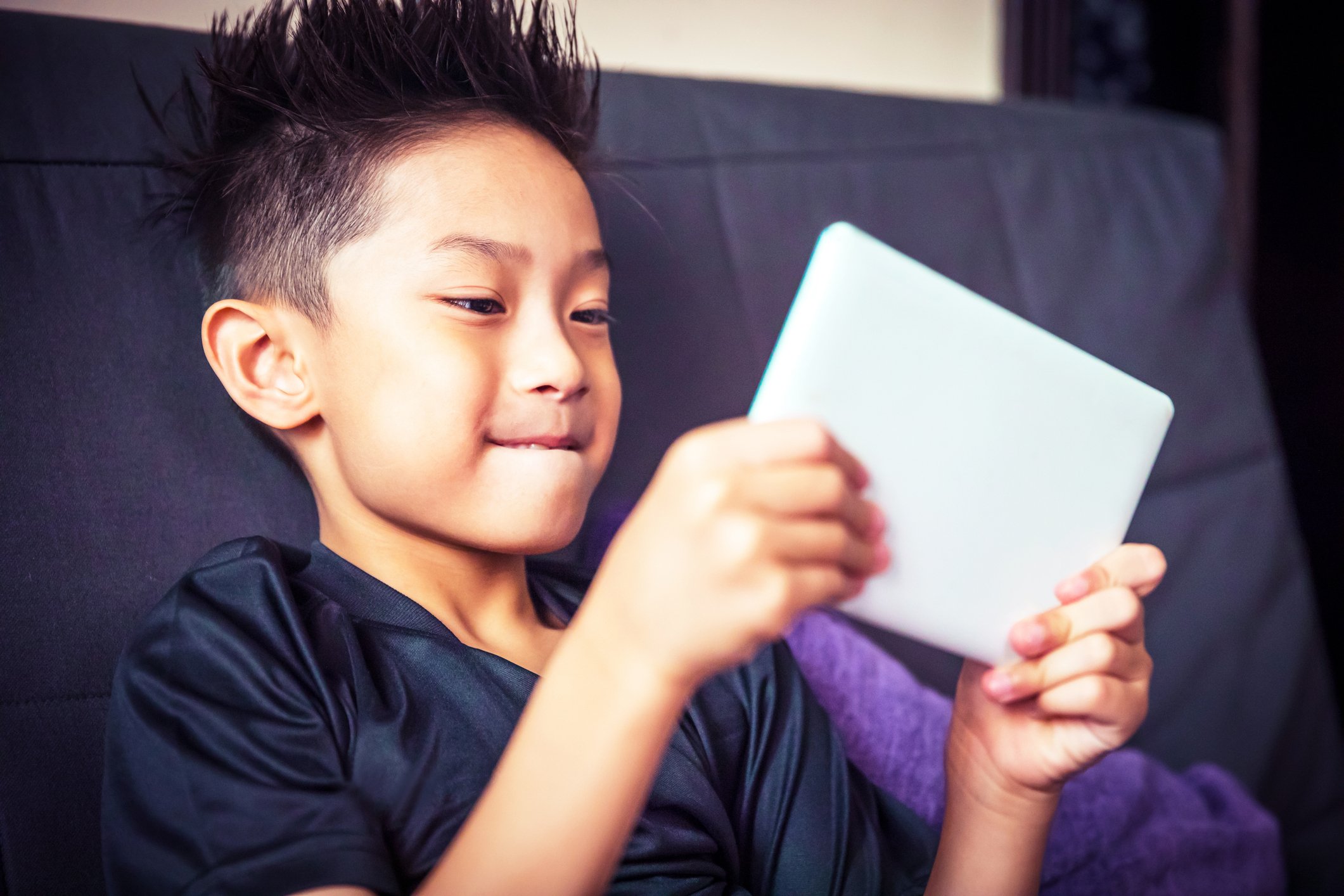 A kid holding a tablet while sitting on a couch.