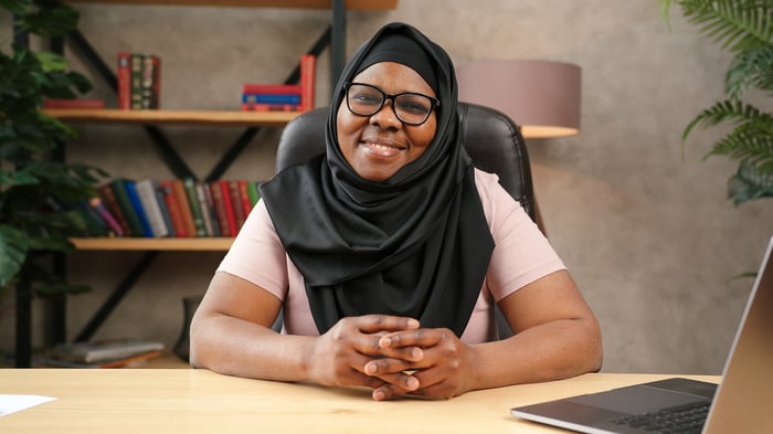 A woman at a desk near an open laptop is smiling at us.