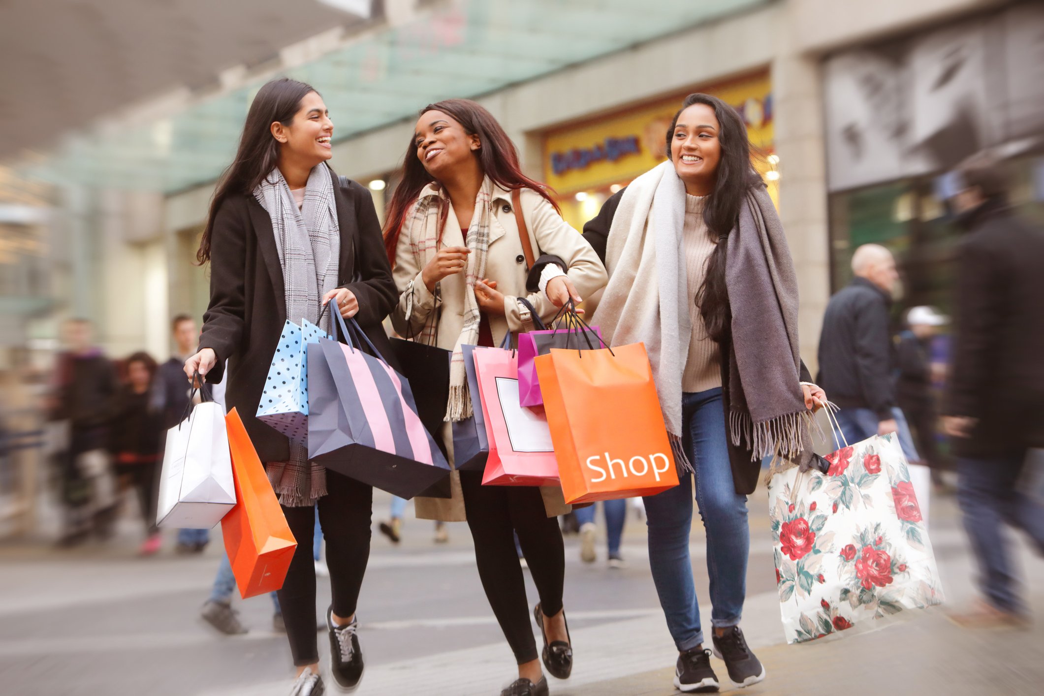 Three people holding shopping bags and walking through a mall.