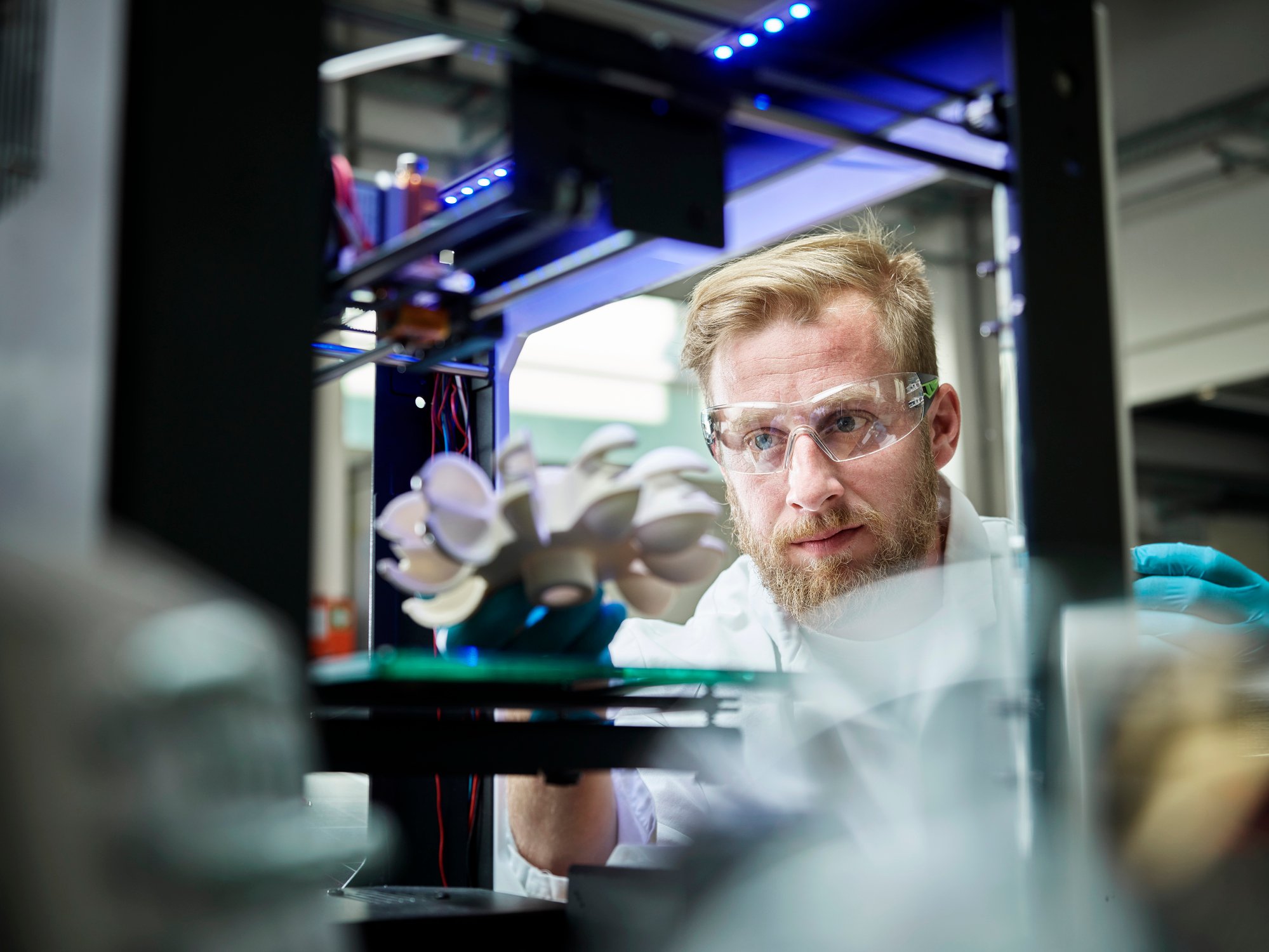 A technician looks at a metal object in a 3D printer. 