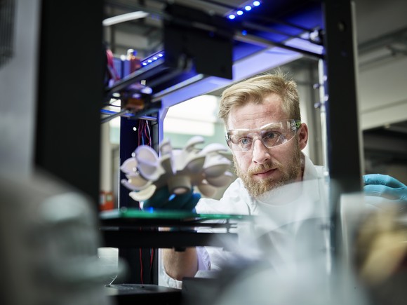 A technician looks at a metal object in a 3D printer. 