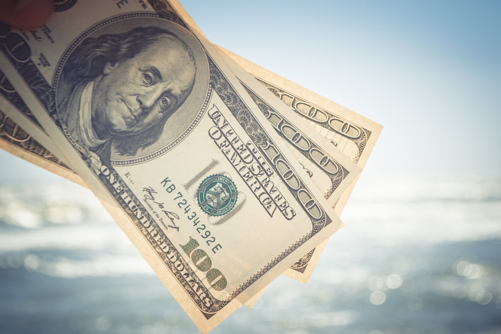 Three $100 bills in front of a body of water.