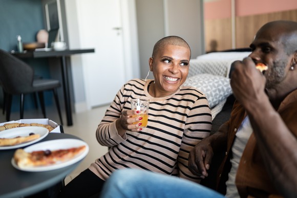 A smiling couple eating pizza by the couch.