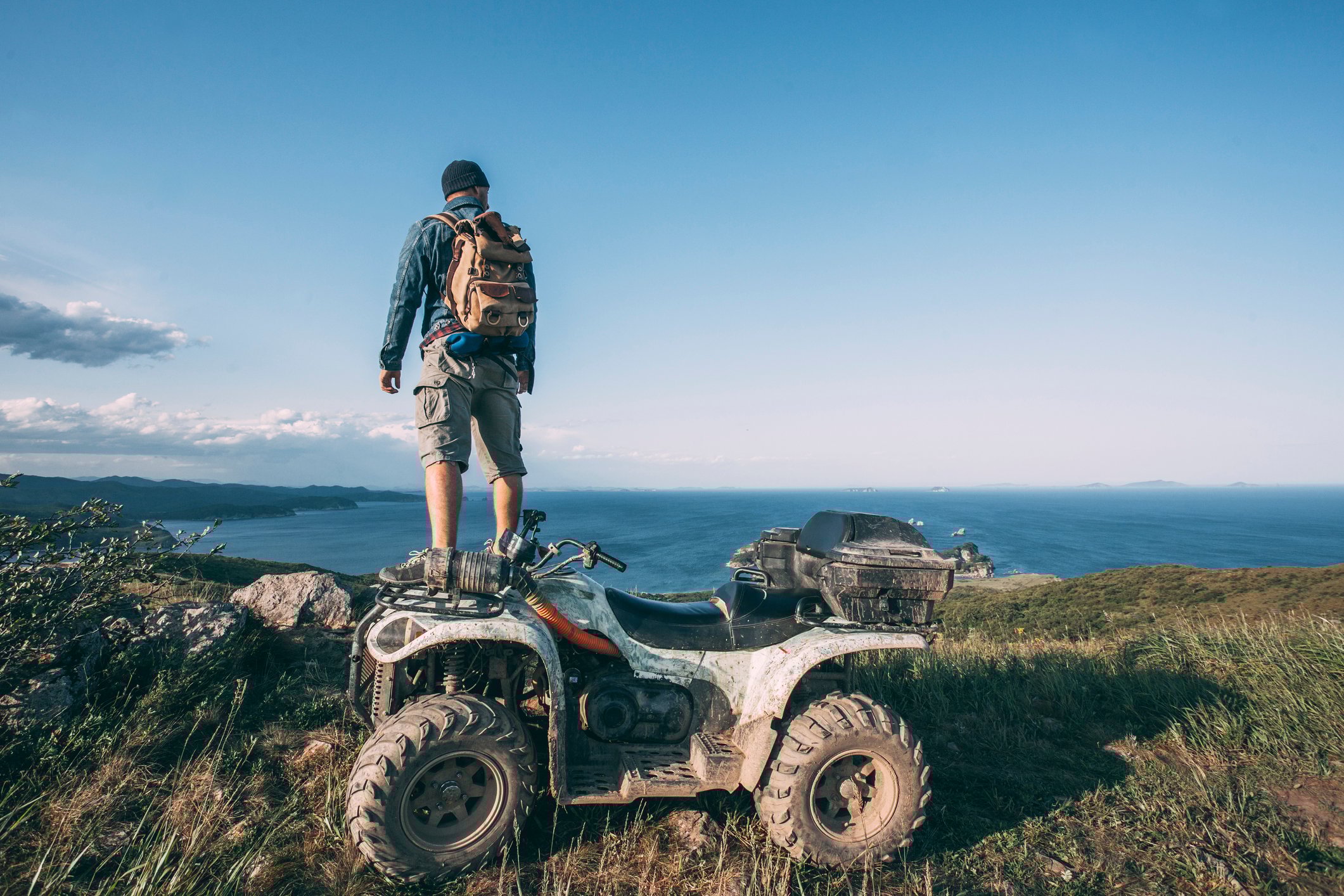 A man standing on an ATV looking out over the ocean.
