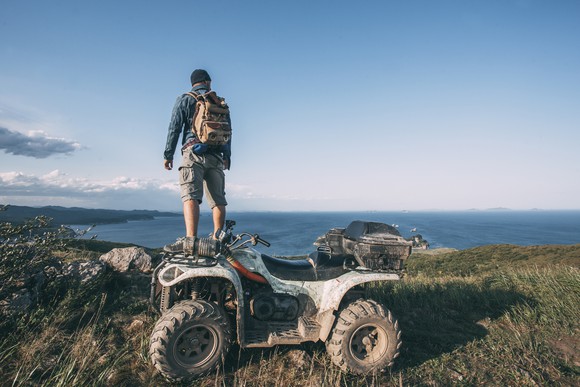 A man standing on an ATV looking out over the ocean.