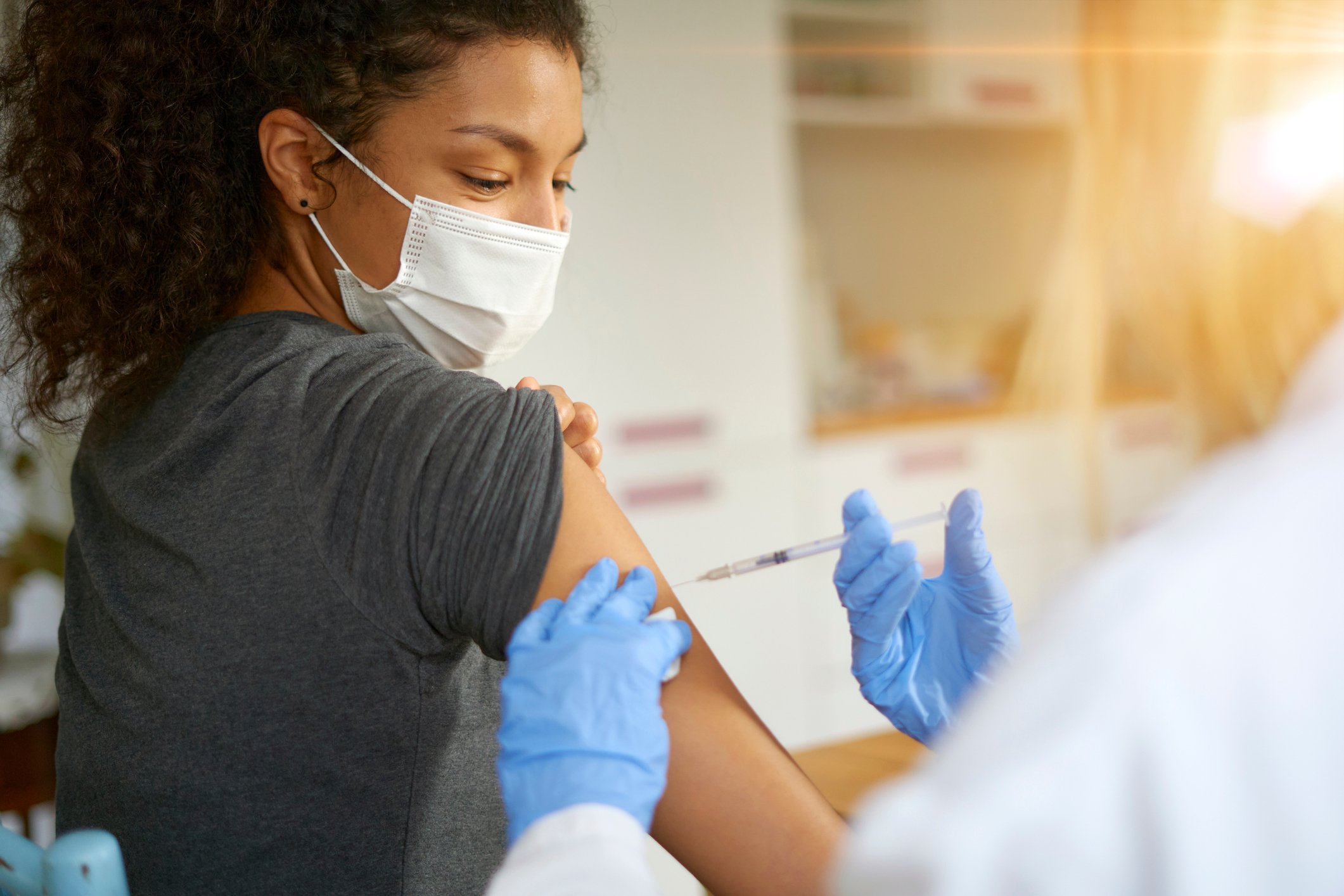 A masked woman with a rolled-up sleeve receives an injection.