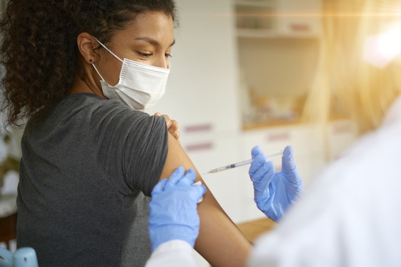 A masked woman with a rolled-up sleeve receives an injection.