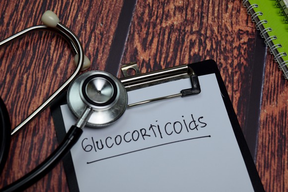 A stethoscope rests on a clipboard holding a paper headed Glucocorticoids.