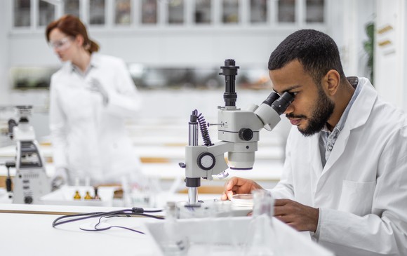 Two scientists in a lab with one scientist looking through a microscope.