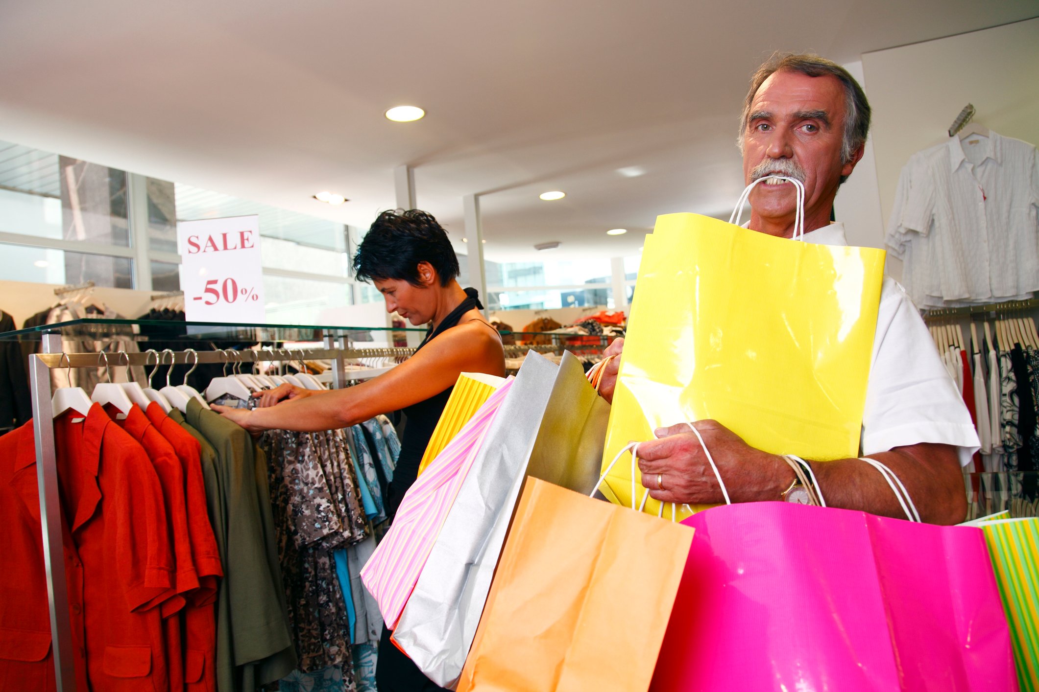 A couple shopping, with a man carry an overwhelming number of bags.