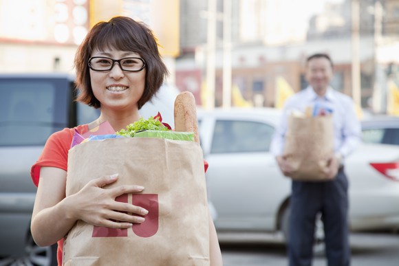 Two people hold brown paper bags full of groceries. 