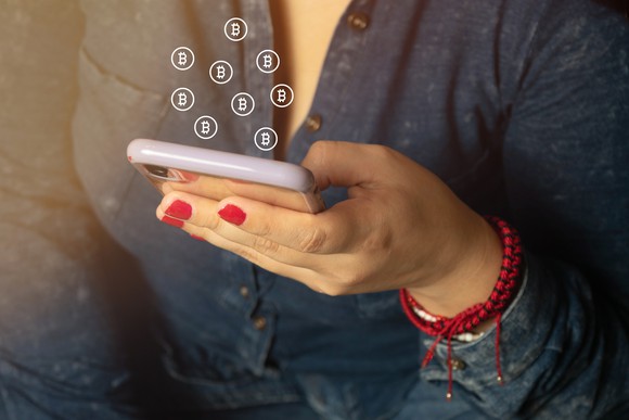 Closeup of woman's hand operating smartphone and Bitcoin icons coming out. 