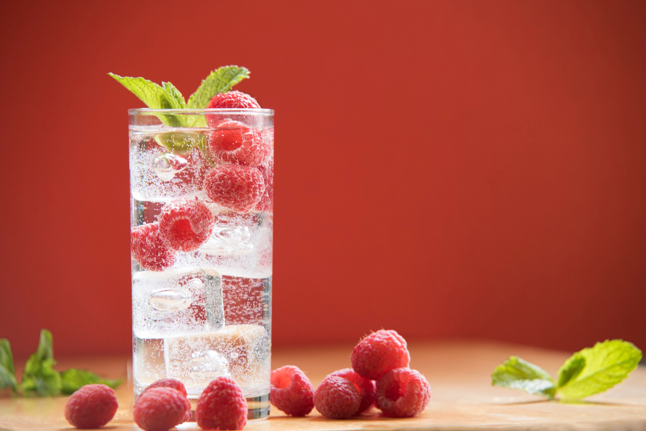 Raspberries around glass of seltzer