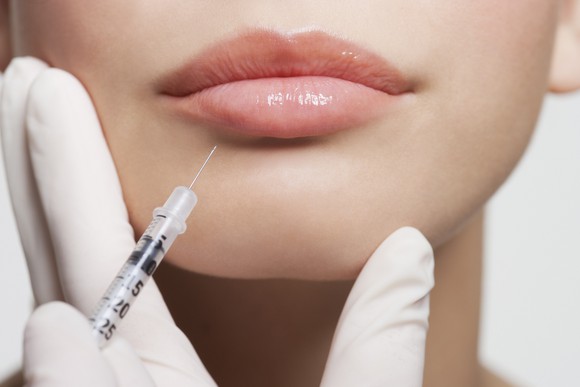 A syringe pointing at a person's lips.
