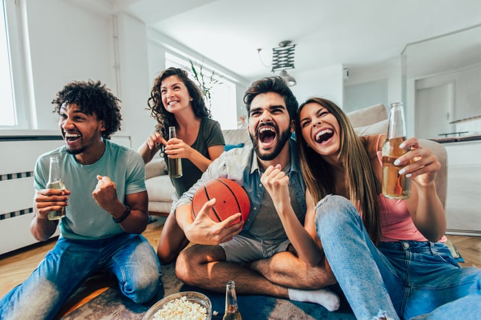 People sitting in a living room, drinking from bottles, as one of them holds a basketball.