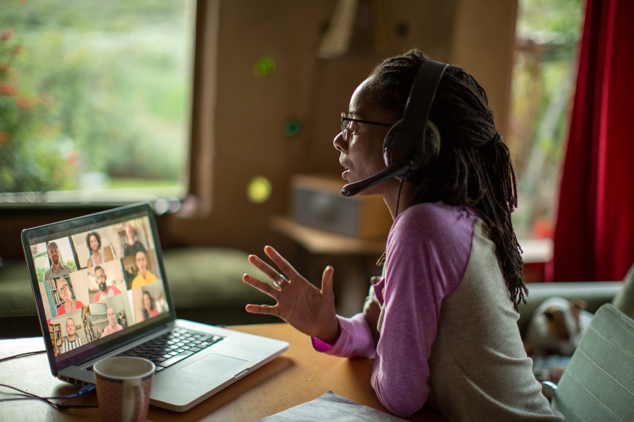 A person at a table wearing headphones with a mouthpiece videoconferencing. 