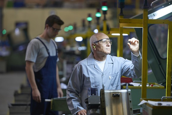 A factory employee inspects a small part under a work light