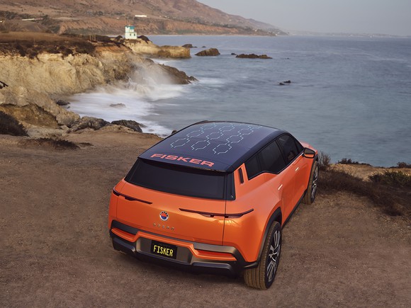 An orange Fisker Ocean parked on a clifftop overlooking the sea, showing its solar panel roof. 