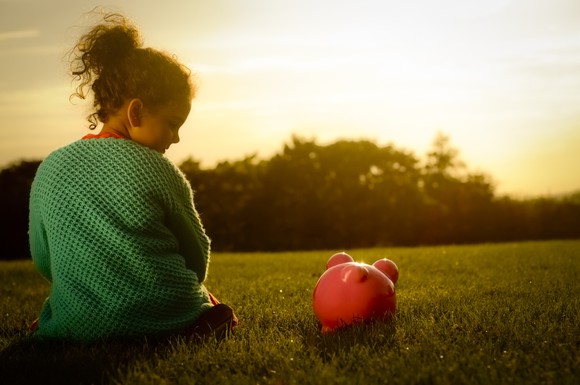 A girl looks down at her piggy bank while the sun sets in the background. 