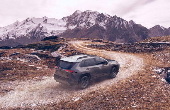 A Toyota RAV4 driving on a dirt road, with snow-capped mountains in the background.
