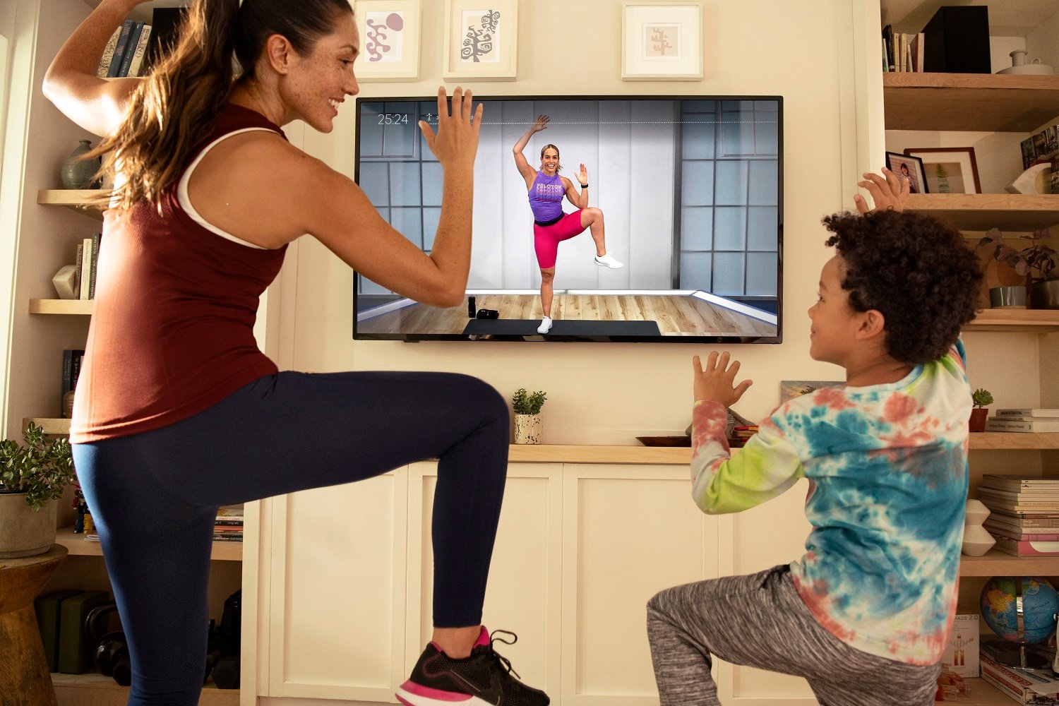 A parent and a child exercise together following instructions from video content.