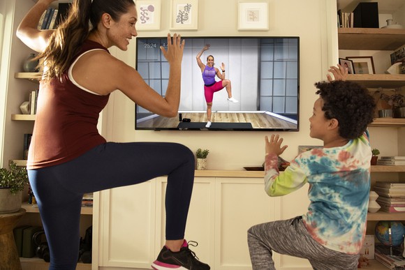 A parent and a child exercise together following instructions from video content.