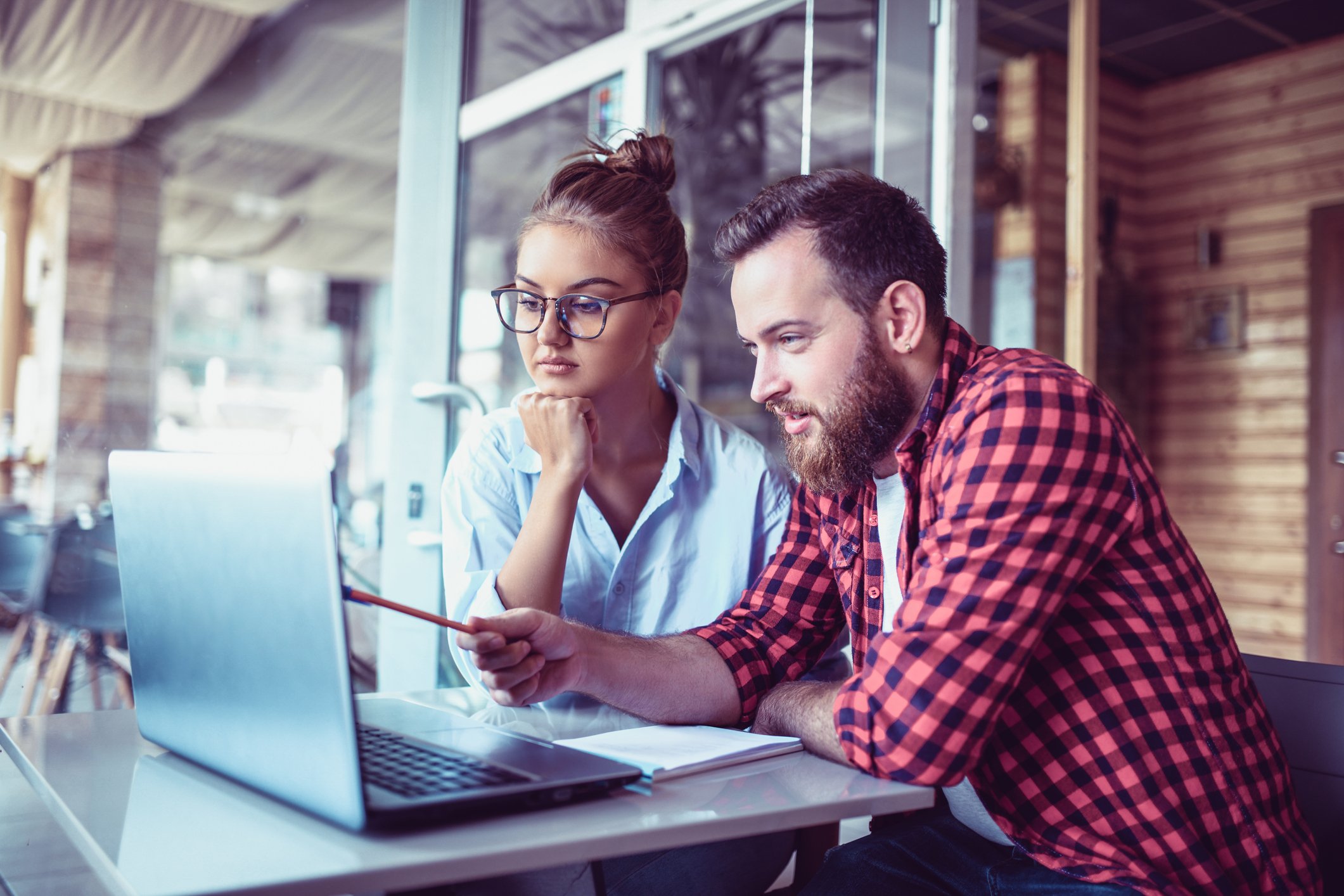 Two people sitting at a table look at a laptop computer together. 