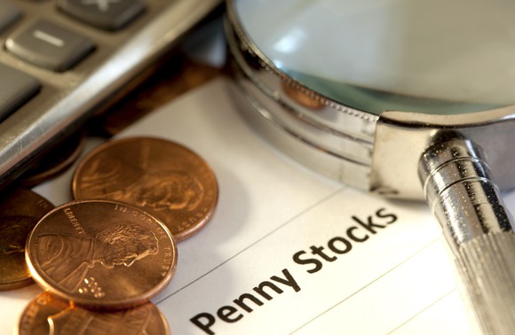 Pennies next to a document with Penny Stocks printed on it and a magnifying glass on top of it.