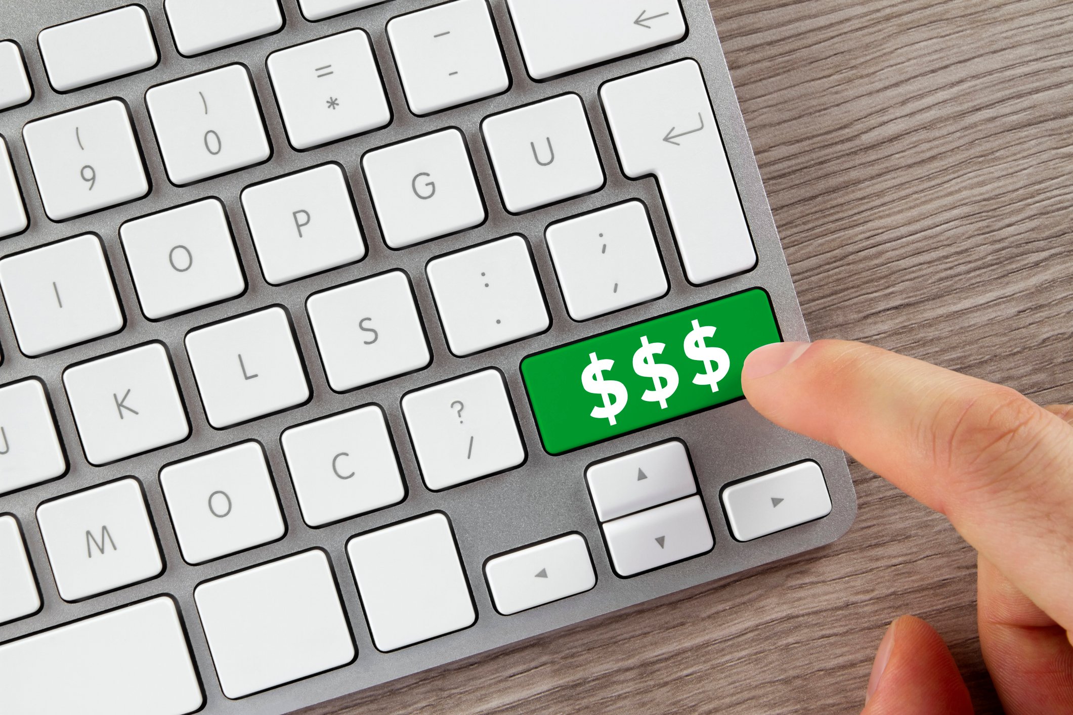 An index finger on top of a green button on a computer keyboard with three dollar signs on the button.