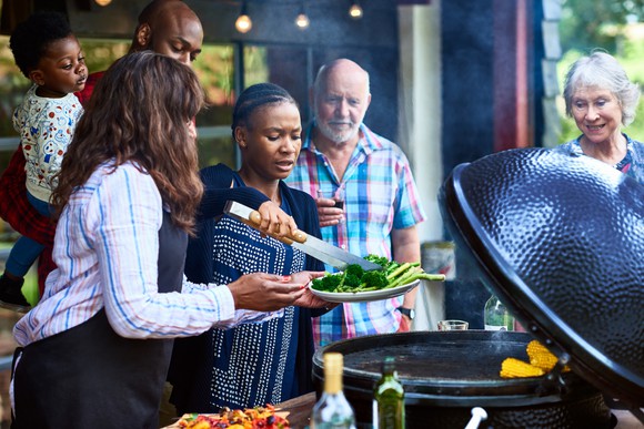 A group of people cooking and serving food off a grill.