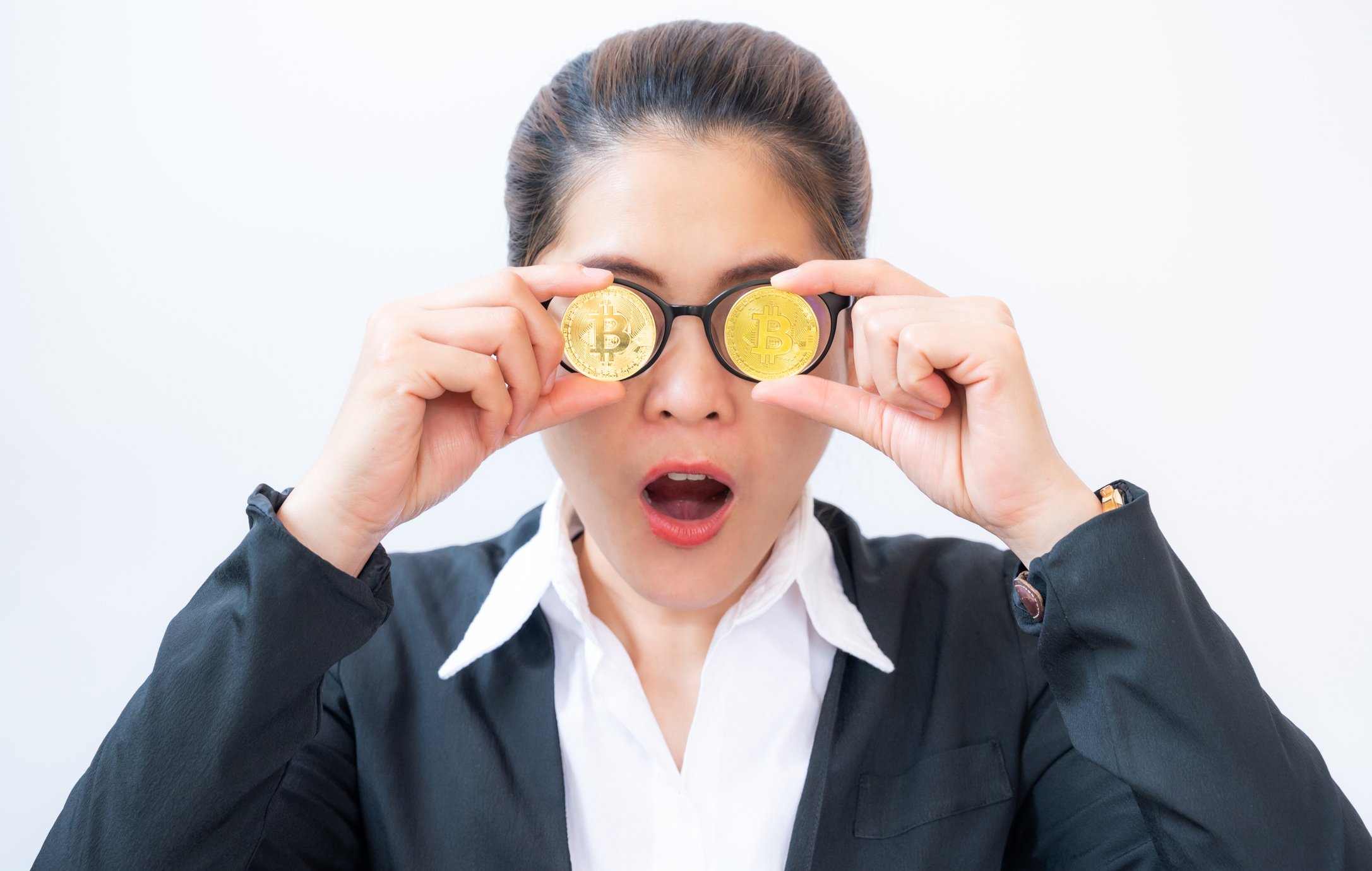 Person holding two gold-colored coins with Bitcoin symbol in front of eyeglasses.