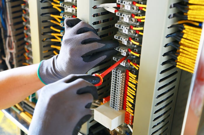 Gloved hands work on a box of electrical wiring.