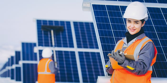 Two workers in reflective vests stand near solar panels.