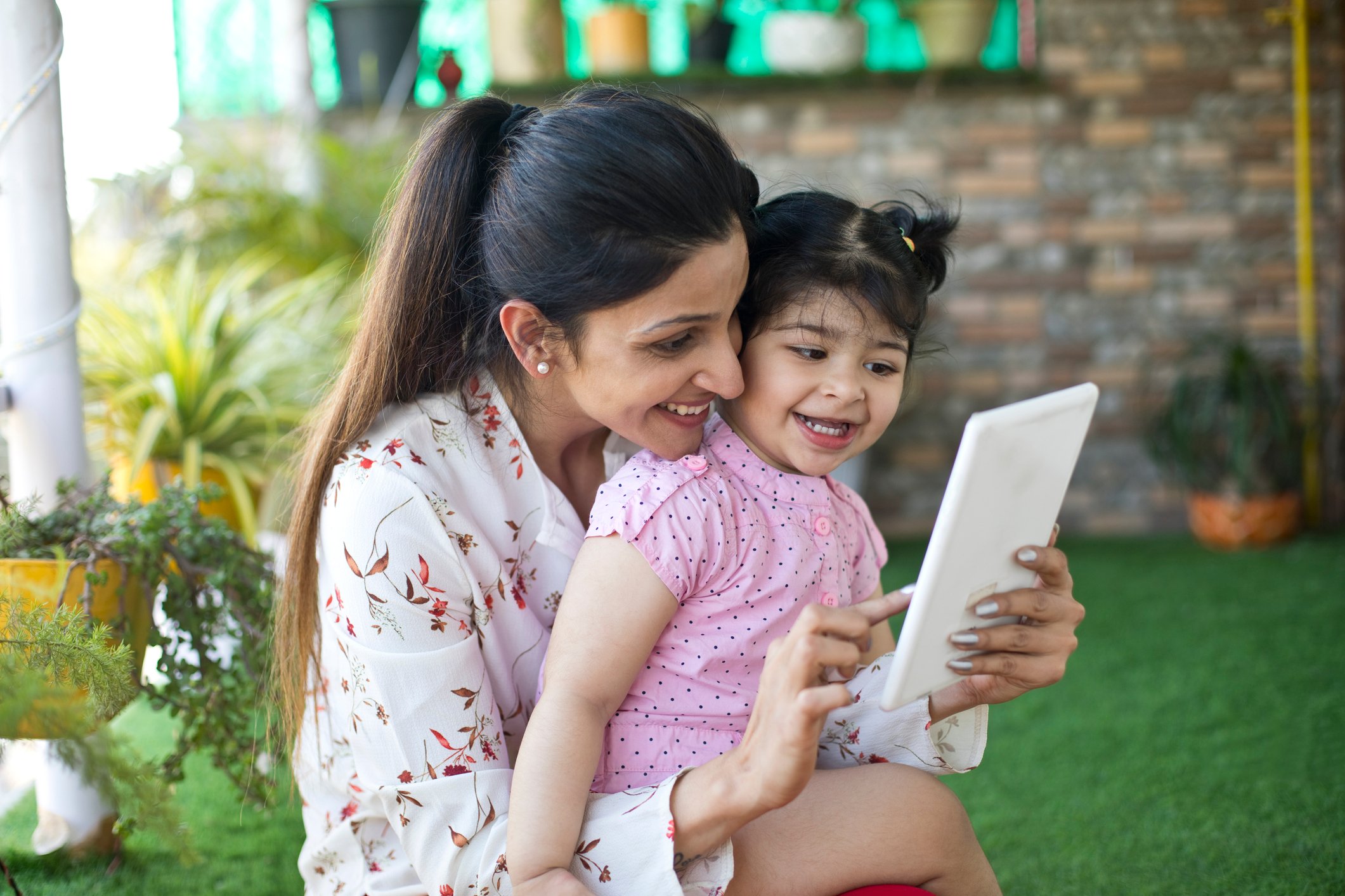 a mother and a toddler smile while looking at a tablet computer.
