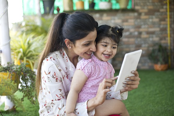 a mother and a toddler smile while looking at a tablet computer.