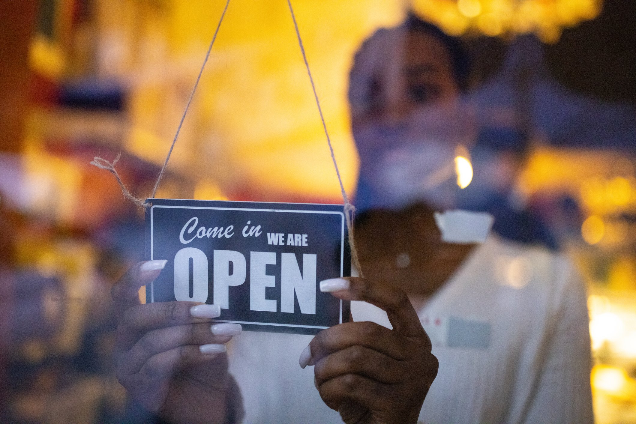 A store owner hangs an open sign on a glass window.