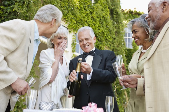 Five people toasting with a bottle of champagne in front of a luxury home.