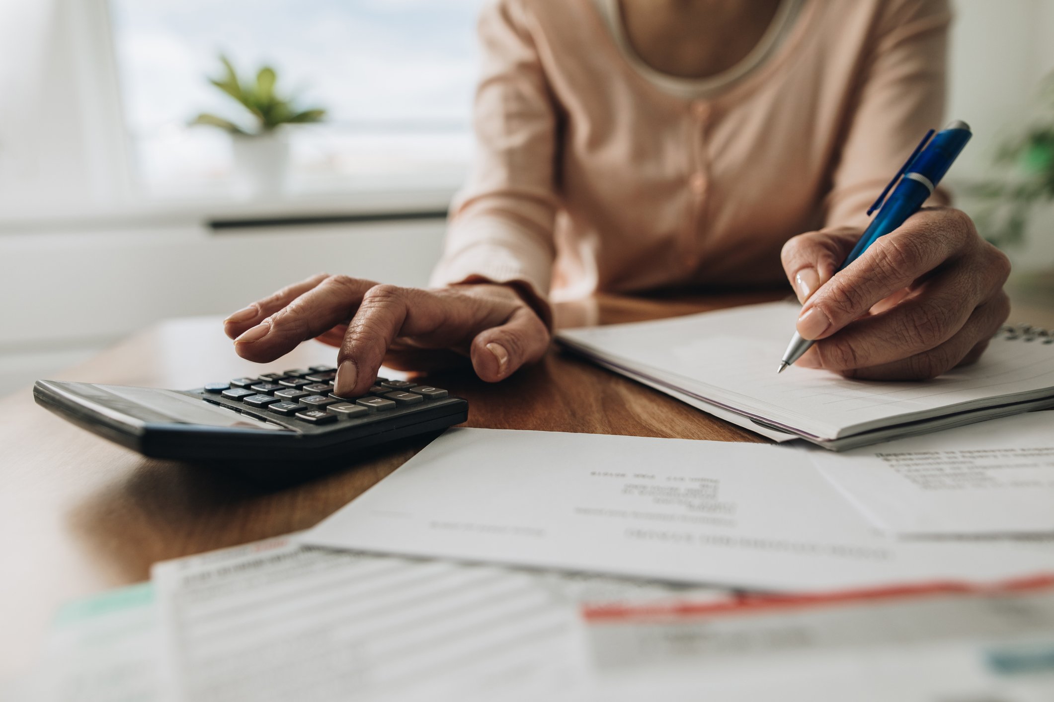 A person tapping a calculator at a table, surrounded by paperwork.