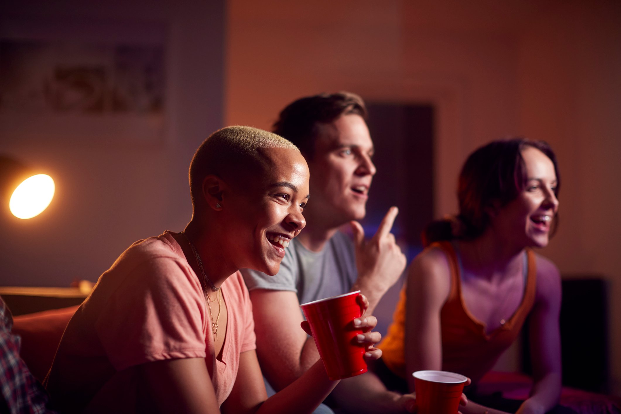 group of friends with drinks sitting on sofa watching a movie