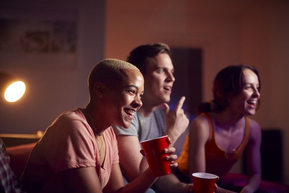 group of friends with drinks sitting on sofa watching a movie
