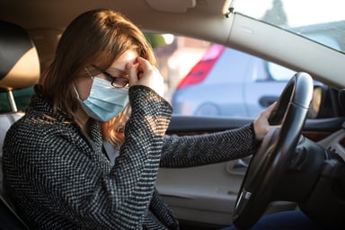 An anxious person in a mask waiting inside a car.
