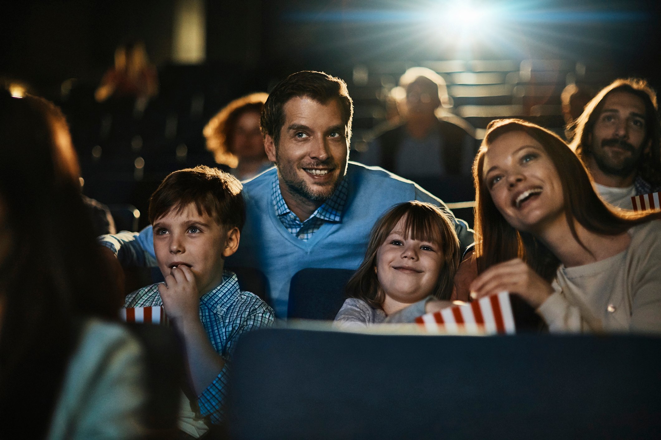 Two adults and two children eat popcorn and watch a movie in a theater.