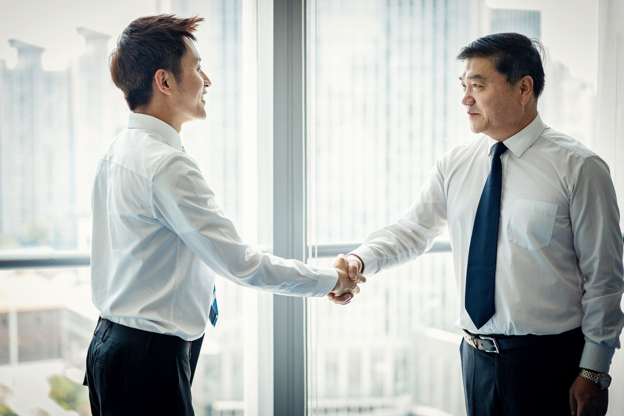 Two people in business attire shaking hands while standing up.