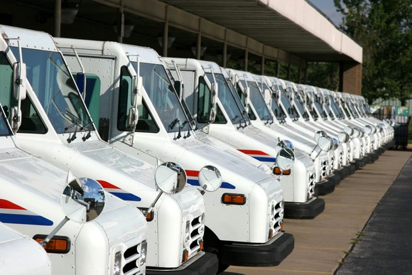 USPS delivery vehicles parked in a row outside a building.