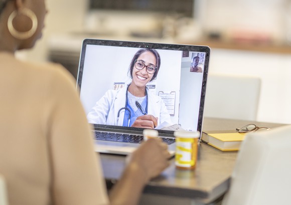 A person with pill bottles looking at a laptop showing a smiling physician.