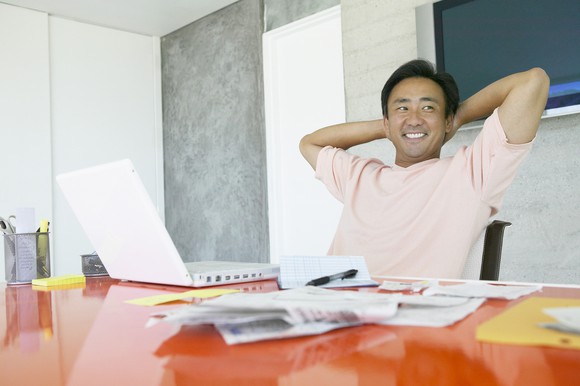Smiling person sitting behind desk with laptop and papers on it.
