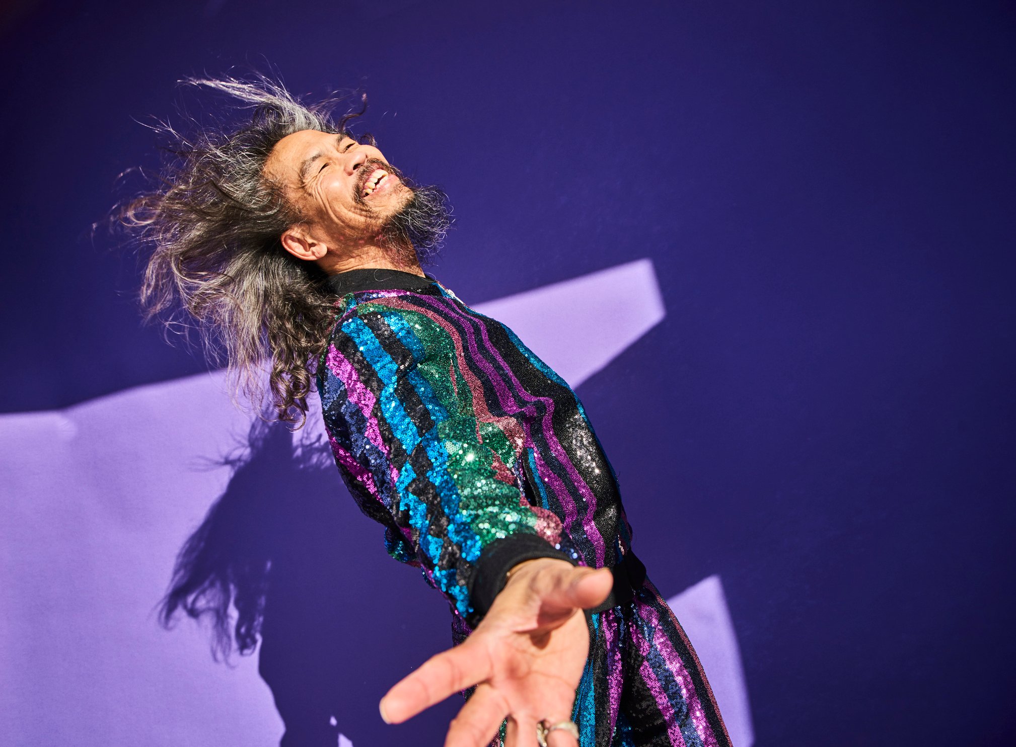 happy person in colorful disco outfit dancing against purple background